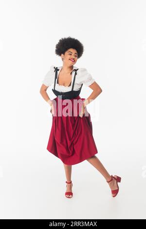 overjoyed african american oktoberfest waitress in traditional bavarian costume dancing on white Stock Photo