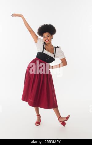 excited african american oktoberfest waitress posing in bavarian dirndl on white, full length Stock Photo