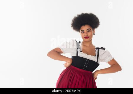 confident african american oktoberfest waitress in traditional attire with hands on hips on white Stock Photo