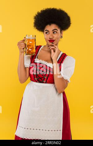 tricky african american oktoberfest waitress in dirndl costume standing with beer mug on yellow Stock Photo