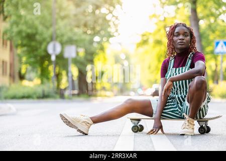 Portrait of a black non-binary person with a skateboard sitting on the street Stock Photo