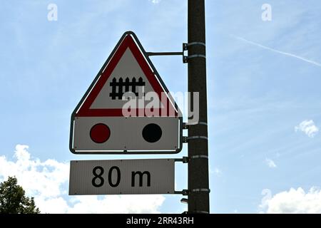 Three traffic signs arrange vertical are meaning railroad crossing ahead with barrier or gate with traffic light in distance of 80 metres. Stock Photo