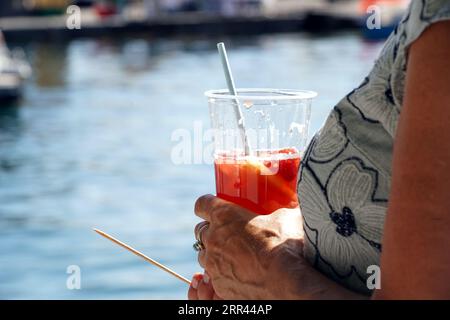 Plastic glass with strawberry drink and paper straw inside holding by woman. Stock Photo