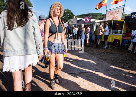 A woman with a furry hat, shorts and a pint of beer among the food stalls at Green Man Festival, Brecon, Wales, UK, 2023. Photo: Rob Watkins Stock Photo