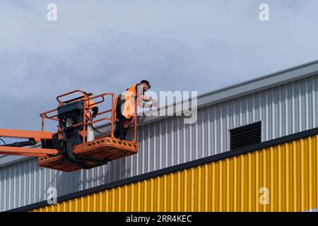 Workers using construction equipment fix roofing on a new factory warehouse building in Melbourne, Australia. Stock Photo
