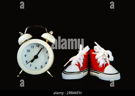Alarm clock and sneakers on a black background. The concept of sport and healthy lifestyle. Stock Photo