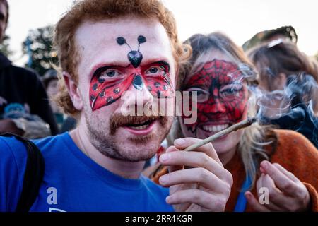 A couple in face paint smoke a huge roll up cigarette in the main field at Green Man Festival, Brecon, Wales, UK, 2023. Photo: Rob Watkins Stock Photo