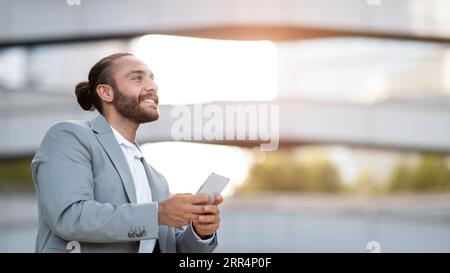 Smiling Handsome Young Businessman With Smartphone In Hands Standing Outdoors Stock Photo