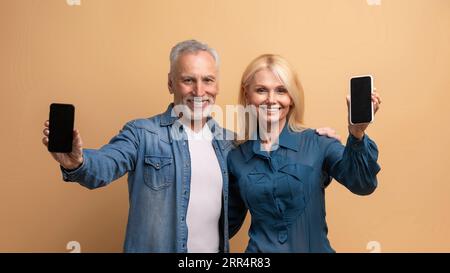 Cheerful elderly man and woman showing phones with mockup Stock Photo