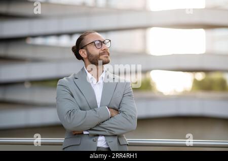 Handsome young businessman in suit standing with arms crossed outdoors Stock Photo