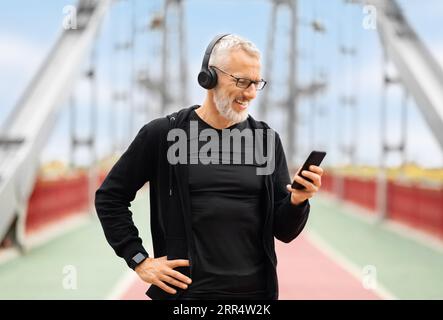 Elderly sportsman using phone while outdoor workout on walking bridge Stock Photo