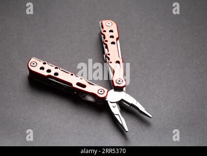 universal multifunctional knife pliers with different nozzles and a red handle on a black background. Versatile camping knife. Multifunctional tool. Stock Photo