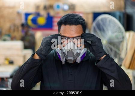 201221 -- KUALA LUMPUR, Dec. 21, 2020 -- Mohamad Hafiz Johari puts on protective gear before working at Kawood workshop on the suburbs of Kuala Lumpur, Malaysia, Dec. 17, 2020. Mohamad Hafiz Johari, together with two other former photographers Abdul Razak Abdul Latif and Noor Adzrene Mohd Noor, came together to set up Kawood, a combination of the Malay word kawan friend and wood, with all three having lost their source of income due to disruptions caused by the COVID-19 pandemic. Undeterred, they brainstormed some means of making a living, ultimately deciding on putting their enthusiasm for co Stock Photo