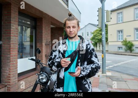 Young male with phone an electronic cigarette standing on motorcycle on city Stock Photo