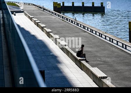 Berlin, Germany. 06th Sep, 2023. A woman sits by the river Spree at the East Side Gallery. Credit: Jens Kalaene/dpa/Alamy Live News Stock Photo