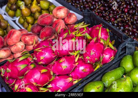 A fruit stall at the Dezerter Bazaar in Tbilisi, Georgia, with dragon fruit (pitahaya, Selenicereus undatus) in the foreground, alongside peaches, figs, cherries and green fruits. The juxtaposition of imported tropical fruits and local summer fruits from the Caucasus reflects the variety of produce on offer at the Georgian capital’s largest food market. Mikheil Tsinamdzghvrishvili Street, Chughureti, Didube, Tbilisi, 0102, Georgia Stock Photo