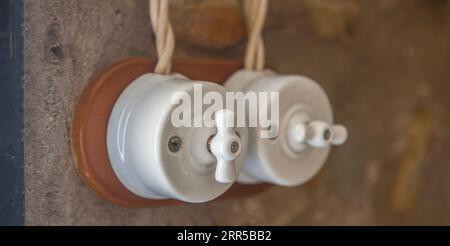 Vintage style double light switch made of porcelain and wood over dry stone wall. Warm light Stock Photo
