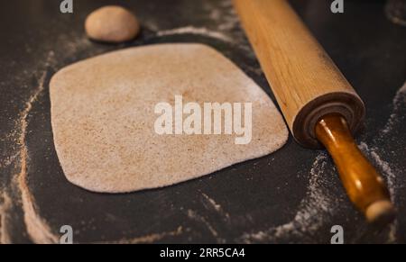 Rolled out wholemeal dough, wheat, grain with vintage rolling pin on the table. Homemade organic dough. Rolled dough on the table. Stock Photo