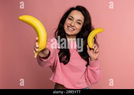 Smiling young woman posing with her favorite unpeeled yellow fruit during the photo shoot in a studio. Healthy eating concept Stock Photo