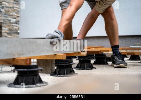 Low angle view of a man, a worker, leveling a supportive construction for wooden terrace or patio with a long label tool. Stock Photo