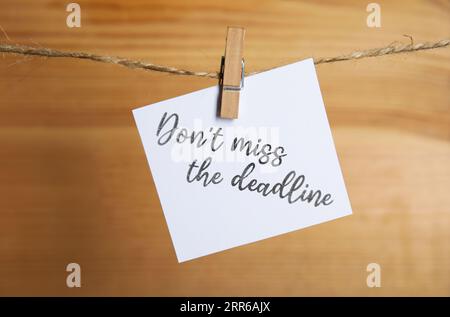 Note with reminder Don't Miss The Deadline hanging on twine against wooden background Stock Photo