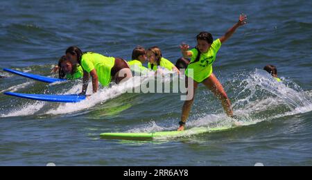 Gilgo Beach, New York, USA - 25 July 2023: Kids in neon green shirts riding on waves while surfing at Bunger Surf Camp at Gilgo Beach on Long Island. Stock Photo