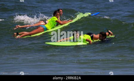 Gilgo Beach, New York, USA - 25 July 2023: Kids in neon green shirts riding on waves while surfing at Bunger Surf Camp at Gilgo Beach on Long Island. Stock Photo