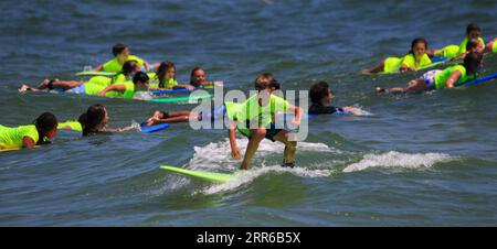 Gilgo Beach, New York, USA - 25 July 2023: Kids in neon green shirts riding on waves while surfing at Bunger Surf Camp at Gilgo Beach on Long Island. Stock Photo