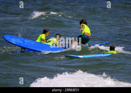 Gilgo Beach, New York, USA - 25 July 2023: Kids in neon green shirts riding on waves while surfing at Bunger Surf Camp at Gilgo Beach on Long Island. Stock Photo