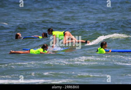 Gilgo Beach, New York, USA - 25 July 2023: Kids in neon green shirts riding on waves while surfing at Bunger Surf Camp at Gilgo Beach on Long Island. Stock Photo