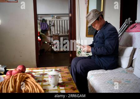 210214 -- YINCHUAN, Feb. 14, 2021 -- Zhang Junming shops for daily necessities online using smartphone one day before the Chinese Lunar New Year at his new residence at the Binhe Jiayuan relocation site in Yinchuan, northwest China s Ningxia Hui Autonomous Region, Feb. 11, 2021. Zhang Junming, 55, once lived in Hongbaiyang Township, an economic backwater in southern Ningxia. When he was young, Zhang had been severely injured in an accident, and hence suffered from leg disabilities that prevented him from seeking job opportunities in the big cities. So he and his family had to scrape a living o Stock Photo