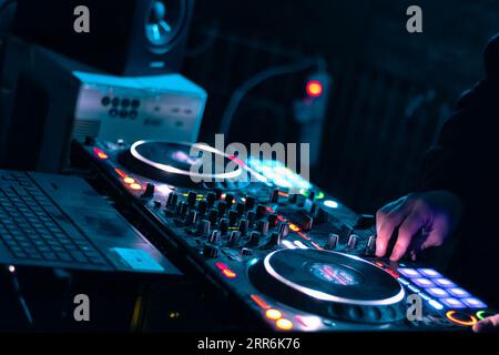 hands of dj playing at an electronic party with colored lights and mixing music on the console Stock Photo
