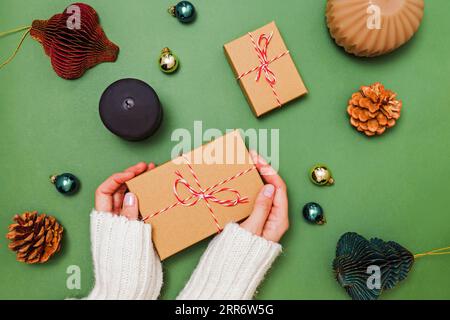 Female hands holding gift box, preparing for holidays, Christmas decor on green table, top view Stock Photo