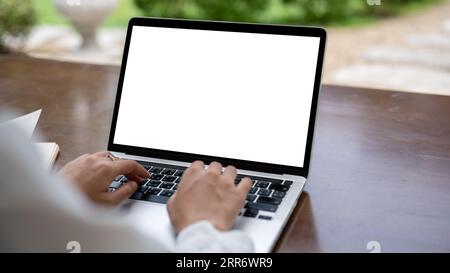 Close-up image of a female freelancer using her laptop computer at a table in a cafe. Laptop white screen mockup for displaying your graphic ads. Stock Photo