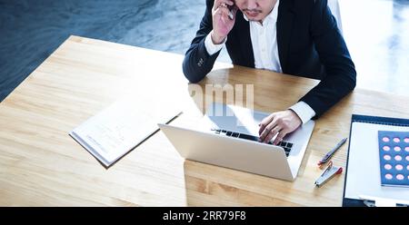 Young businessman sitting in office using smartphone and laptop. Stock Photo
