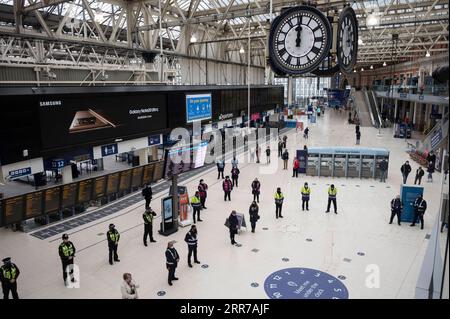 210324 -- LONDON, March 24, 2021 -- Travellers, police officers and rail staff observe one minute s silence at Waterloo Station in London, Britain, on March 23, 2021. Britain on Tuesday marked one year since British Prime Minister Boris Johnson announced the first coronavirus lockdown in the country last year. On March 23, 2020, Johnson unveiled measures to stop the spread of COVID-19. A national minute s silence was held at midday as part of a day of reflection. Britons are also encouraged to stand on their doorsteps at 2000 GMT with phones, candles and torches to remember the past year. Phot Stock Photo