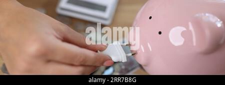 Woman holding power plug and putting on charge pink piggy bank Stock Photo