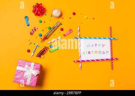 Red ribbon bow aalaw gems streamers sprinkles with happy birthday card gift box yellow backdrop Stock Photo