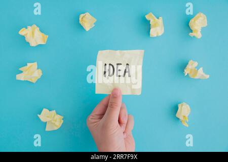Close up person holding idea paper with crumpled ball papers blue backdrop Stock Photo