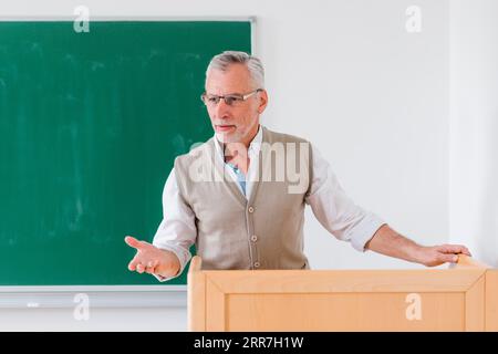 Senior male professor explaining lesson near chalkboard Stock Photo