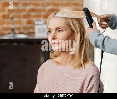 Mature woman getting her hair straightened by hairdresser home Stock Photo