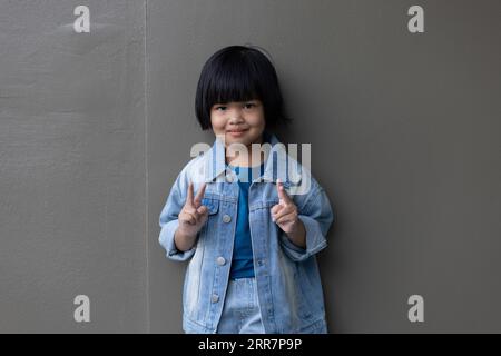 Girl child wearing blue jeans costume standing with her friend on in studio. A sad Girl looking away on grey wall background in family parents house Stock Photo