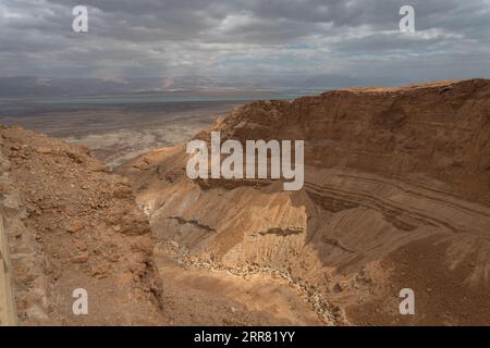 A winding, unpaved road is shown cutting through a barren desert landscape, with a cloudy sky above Stock Photo
