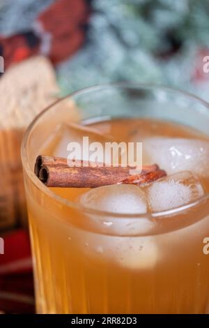 Strong whiskey in a glass with ice and a cinnamon stick with a juniper branch in the background in the Christmas mood. Red black checkered bow on a wo Stock Photo