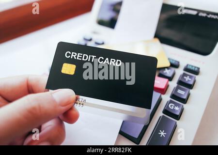 Hand holding credit card with printing calculator on table, black credit card mock in human hand. Credit card and financial concept. Stock Photo