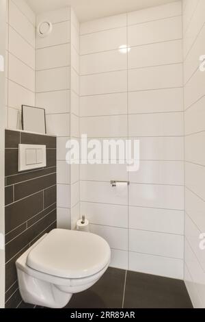 a white toilet in a black and white tiled bathroom with dark tiles on the floor, walls and wallpapers Stock Photo