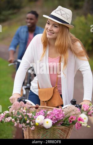 young mixed race couple riding bicycles with flowers in basket Stock Photo