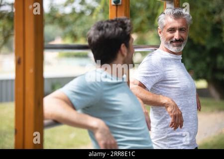 two concentrated sportsmen doing dips on horizontal parallel bars Stock Photo