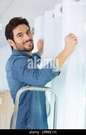 young man installing curtains over window Stock Photo