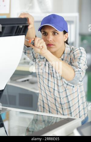 concentrated female repairman repairing broken printer fax machine Stock Photo